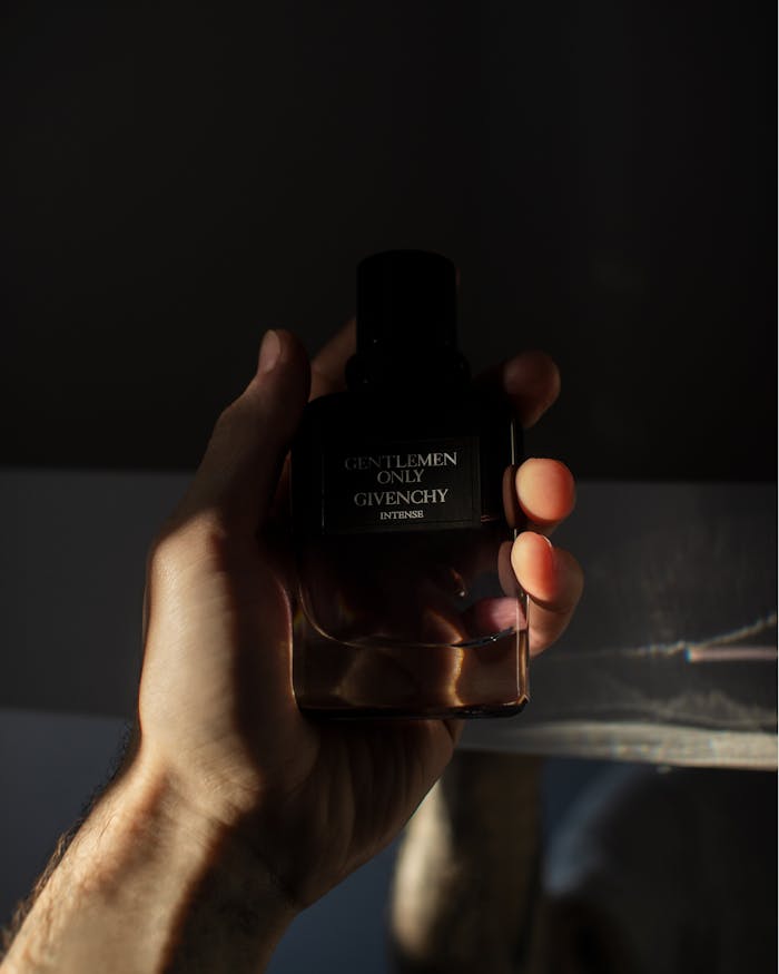 A mans hand holds a Givenchy perfume bottle with dramatic lighting.